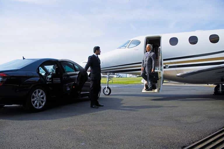 Business traveler stepping off a private jet to a waiting black luxury limo with chauffeur, representing Woodstock airport limo transfer service.