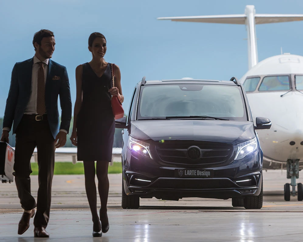 An elegant couple walking towards a luxury vehicle, with an airplane in the background, representing a limousine service from Barrie to Pearson. The man is holding a suitcase, and the woman is carrying a red handbag, both dressed in formal attire, near an executive car that offers a premium airport transfer experience.
